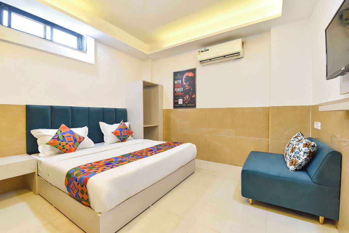 A hotel room with a bed, a sofa, a poster on the wall, and an air conditioning unit.