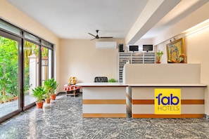 Un comptoir d’accueil d’hôtel avec un logo, un ventilateur de plafond, un téléviseur et une fenêtre donnant sur un paysage verdoyant.