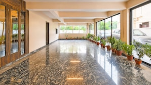 Un amplio pasillo con piso de mármol pulido, ventanas grandes y plantas en macetas a lo largo de las paredes.