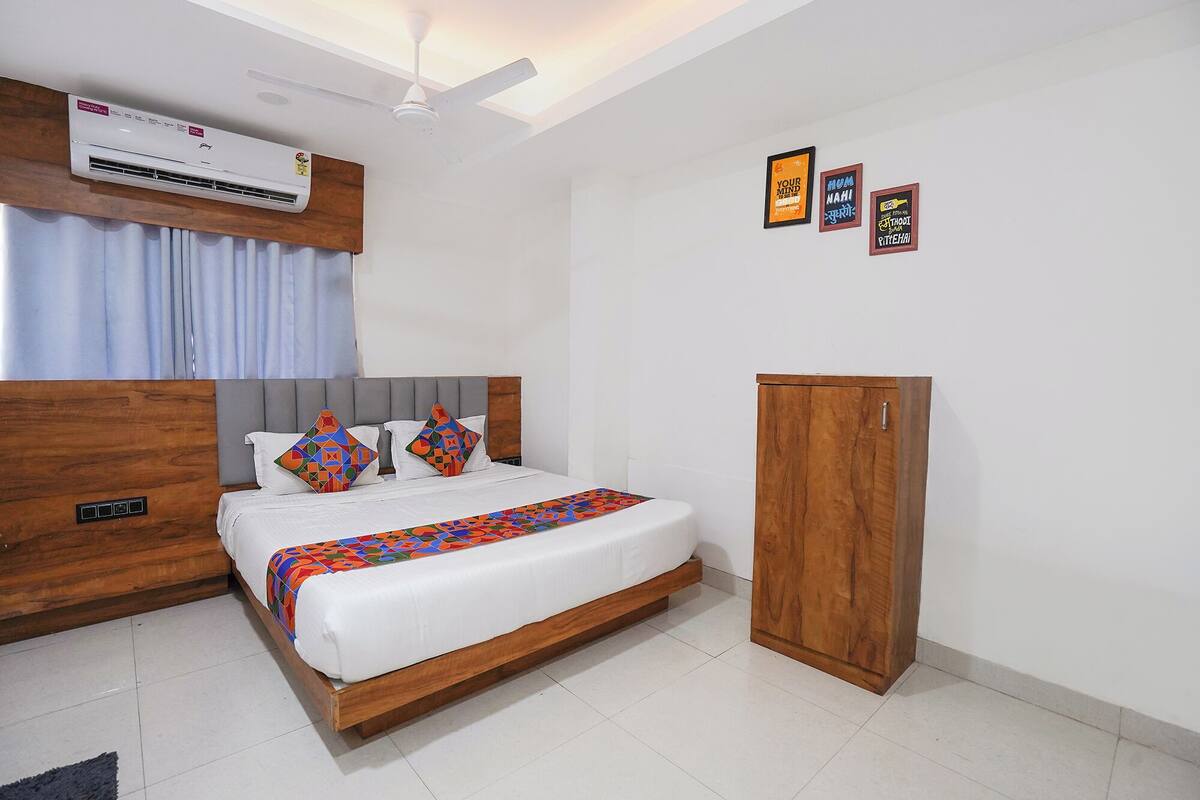A bedroom with a bed, an air conditioner, a ceiling fan, a wardrobe, and a wall with three framed pictures.
