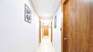 A hallway with white walls, wooden doors, and framed pictures on the walls. - Fabhotel Royal King (Ahmedabad)