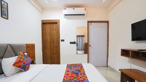 A hotel room with a bed, a TV, a wooden door, and an air conditioning unit. - Fabhotel Royal King (Ahmedabad)