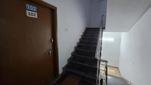 Un escalier avec une rampe, une porte portant l’inscription « 102 », et un luminaire fixé au mur.