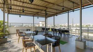 A covered outdoor seating area with tables and chairs, a view of the cityscape, and hanging lanterns. - FabHotel New Rajdoot (Bhopal)