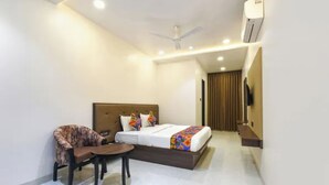 A hotel room with a bed, a chair, a small table, an air conditioning unit, and a television. - FabHotel New Rajdoot (Bhopal)