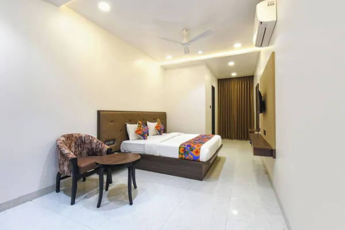 A hotel room with a bed, a chair, a small table, an air conditioning unit, and a television.