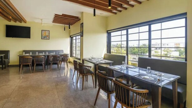 A restaurant with a high ceiling, wooden beams, a large window, and a modern dining area. - FabHotel New Rajdoot (Bhopal)