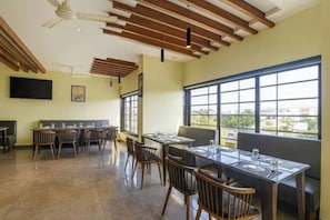 Un restaurante con techo alto, vigas de madera, un ventanal grande y una zona de comedor moderna.