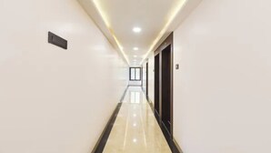 A long, well-lit hallway with a reflective floor, leading to a door at the end. - FabHotel New Rajdoot (Bhopal)