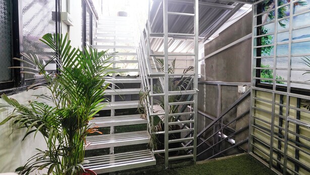 A metal staircase with a metal railing, surrounded by potted plants and a window with a view of palm trees.