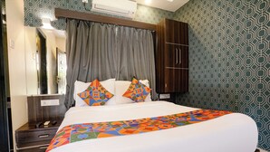 A hotel room with a bed, a wooden wardrobe, a nightstand, and a mirror. - Via Nisarg Blue (Alibag)