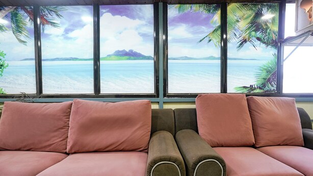 A room with a large window, two sofas with pink cushions, and a view of a calm sea and distant mountains. - Via Nisarg Blue (Alibag)