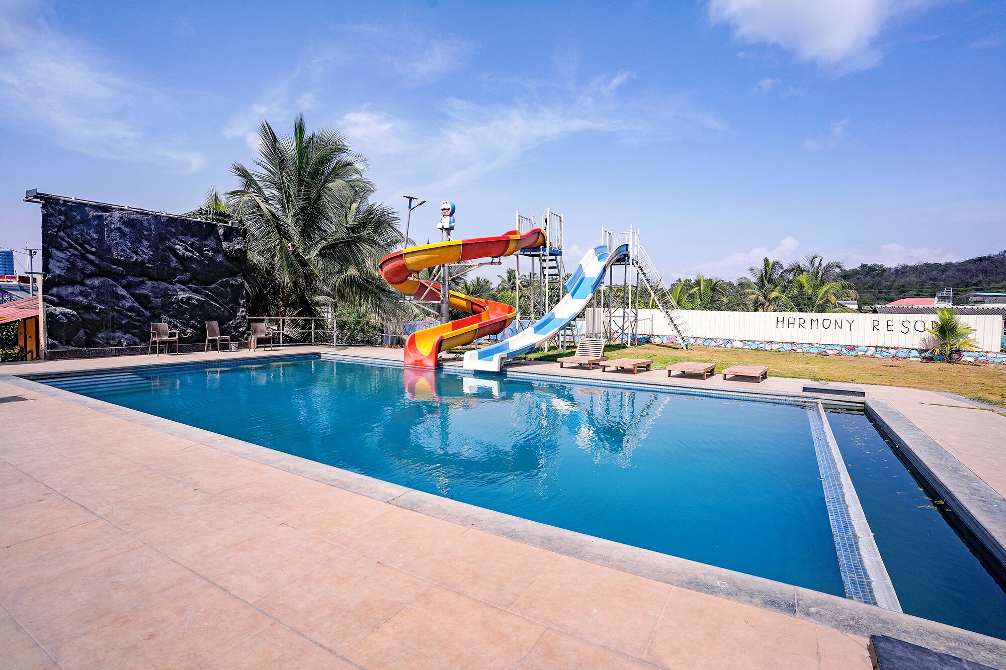 A swimming pool with a water slide, lounge chairs, and a rock wall.