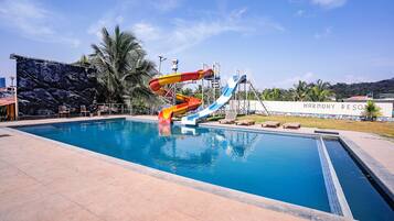 A swimming pool with a water slide, lounge chairs, and a rock wall.