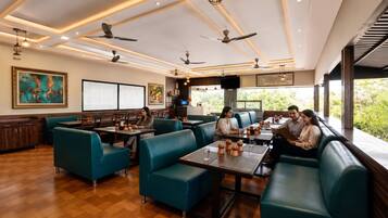 A modern restaurant interior with wooden flooring, teal seating, and ceiling fans.