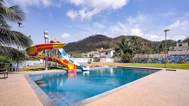 A swimming pool with a water slide, a mountain backdrop, and a sign reading 'HARMONY RE SORT'. - Fabhotel Prime Harmony Resort (Alibag)