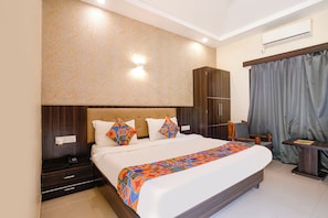 A hotel room with a large bed, a wardrobe, a desk, and a window with curtains.