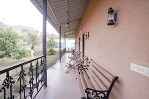 A covered outdoor seating area with benches and a railing, overlooking a landscaped garden.