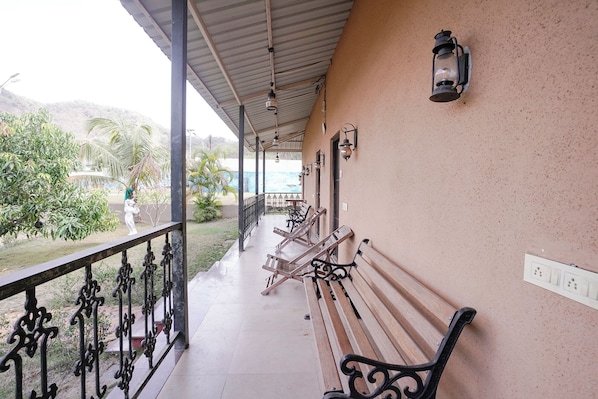 A covered outdoor seating area with benches and a railing, overlooking a landscaped garden.