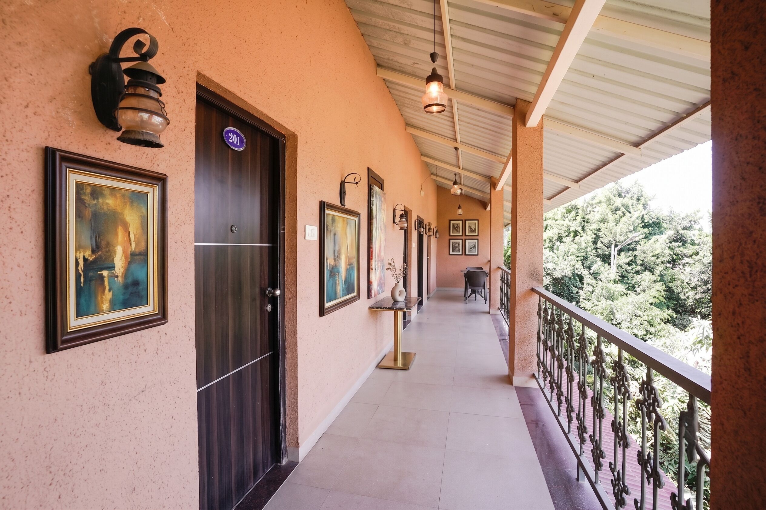 A corridor with a door marked '201', a framed painting, and a view of greenery outside.