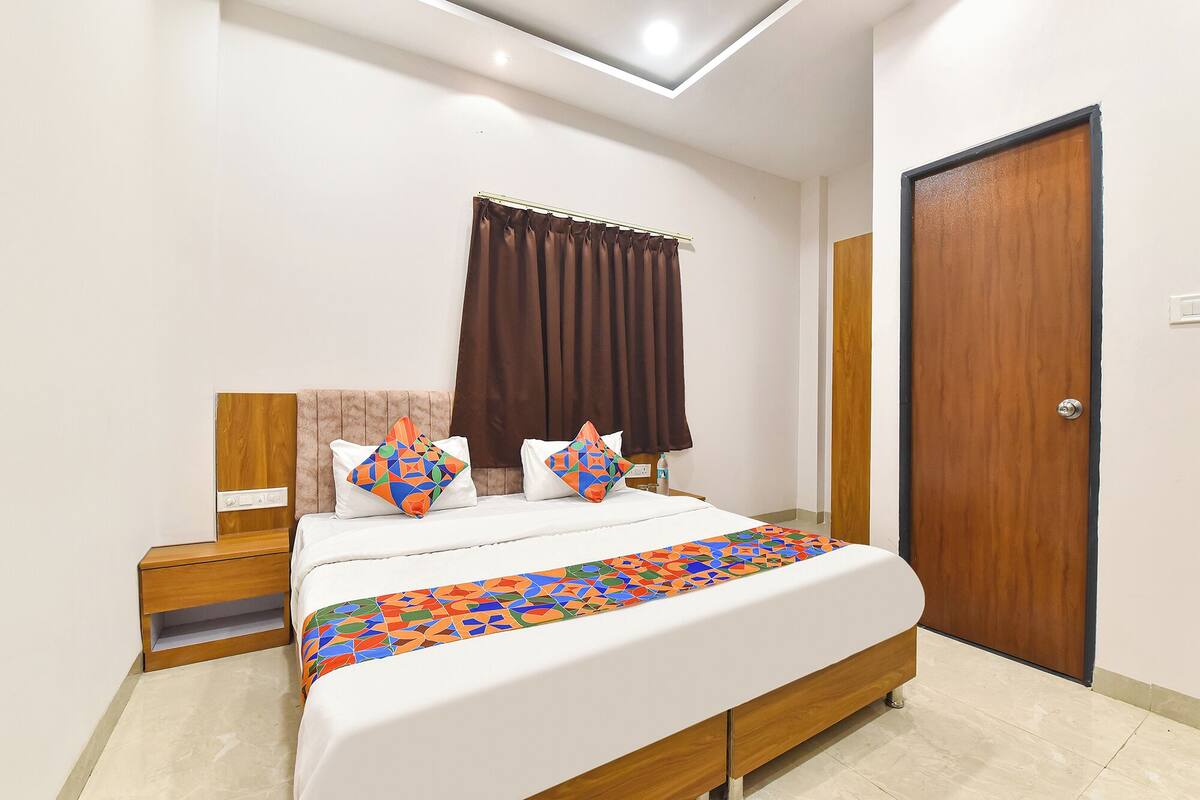 A bedroom with a bed, a wooden nightstand, a door, and a window with curtains.