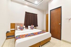 A bedroom with a bed, a nightstand, a wooden door, and a ceiling light. - FabHotel AVR, Mahalaxmi Nagar (Indore)