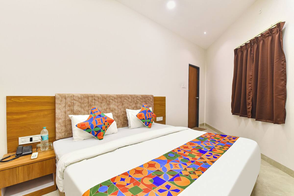 A hotel room with a bed, a nightstand, a phone, and a window with curtains.