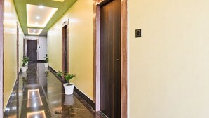 Um corredor de hotel com chão de mármore, plantas em vasos, portas de madeira e teto verde.