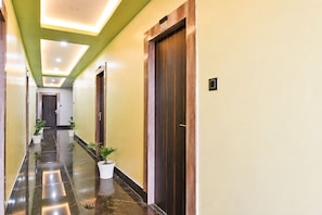 A hotel hallway with a marble floor, potted plants, wooden doors, and a green ceiling. - Fabhotel Prime Tanishq Inn (Barasat)