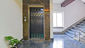 Um corredor com piso de mármore, um portão de metal, um vaso de plantas e uma escada com grades de metal.