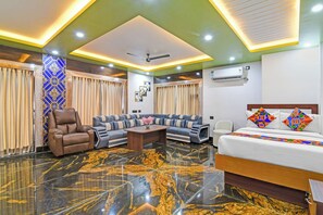 A hotel room with a sofa, a chair, a bed, a coffee table, and a ceiling fan. - FabHotel Prime Tanishq Inn (Barasat)
