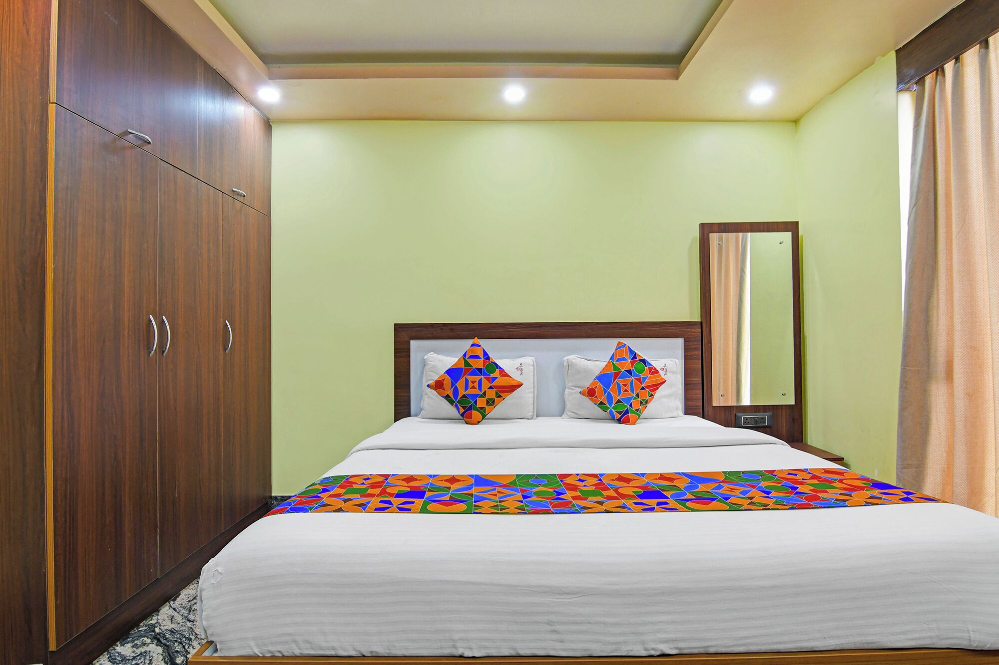 Una habitación de hotel con cama, armario, espejo y ventana con cortinas.