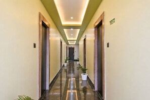 A hotel corridor with a polished floor, wooden doors, and potted plants. - FabHotel Prime Tanishq Inn (Barasat)