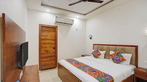 A hotel room with a bed, a wooden door, an air conditioning unit, a ceiling fan, and a bedside table with a water bottle. - FabHotel Southtown - Near Govindpuri Railway Junction (Kanpur)