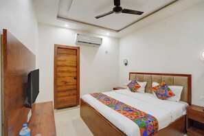 A hotel room with a bed, a wooden door, an air conditioning unit, a ceiling fan, and a bedside table with a water bottle. - Fabhotel South Town - Near Govindpuri Railway Junction (Kanpur)