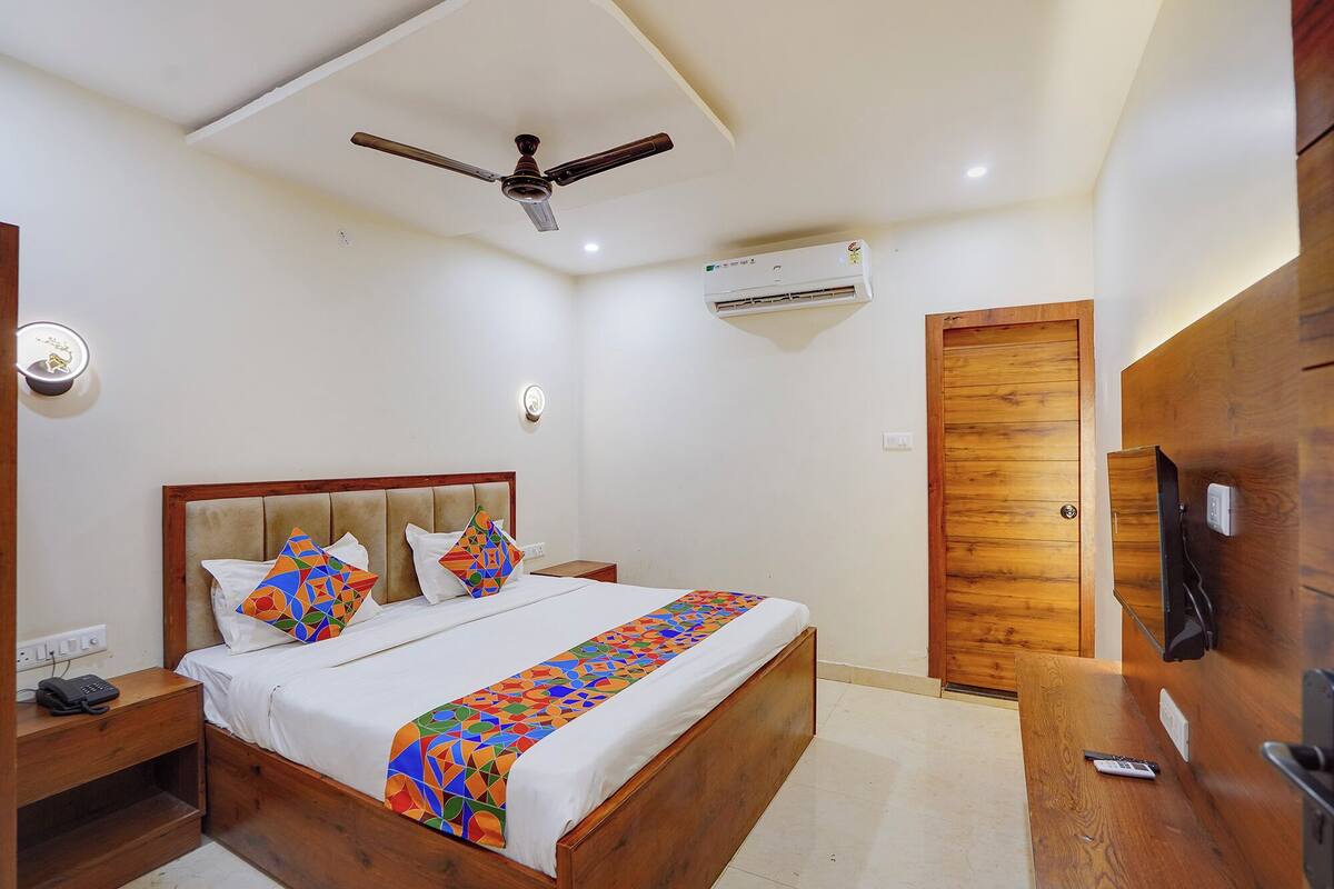Un dormitorio con cama, ventilador de techo, unidad de aire acondicionado, puerta de madera y mesita de noche con teléfono.