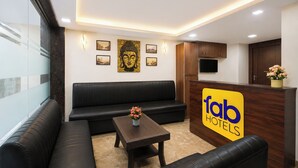 A hotel lobby with a reception desk, a sofa, a coffee table with flowers, and framed pictures on the wall. - FabHotel Karol Bagh Residency - Nr. Karol Bagh Market (New Delhi)