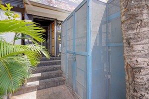 A metal gate with a lock, a staircase leading to a building entrance, and a palm tree in the foreground. - Via Utsav Grand Inn - RR Nagar (Bangalore)