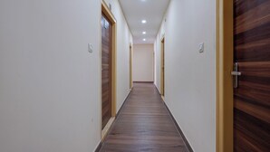 A hallway with wooden doors and white walls, leading to a room. - Via Utsav Grand Inn - RR Nagar (Bangalore)