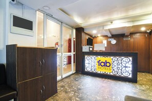 Et hotellets receptionområde med en glasdørindgang, en receptionsdisk med et skilt der siger 'fab hotels', et ur og en brandslukker.