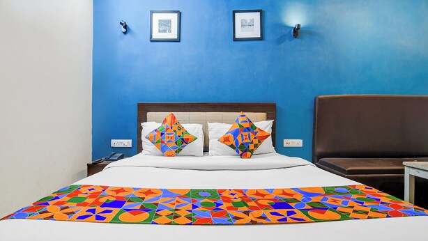 A hotel room with a blue wall, a bed with white bedding, colorful pillows, and a brown leather chair. - Fabhotel Stay Hub (Kolkata)