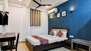 A hotel room with a bed, a desk, a chair, a ceiling fan, an air conditioner, and a wall with a picture. - Fabhotel Stay Hub (Kolkata)