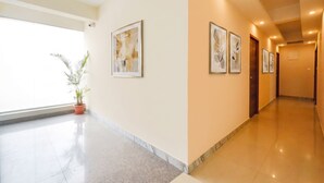 A hotel corridor with framed artwork on the walls, a potted plant, and a polished floor. - FabHotel Fabulous (Bangalore)