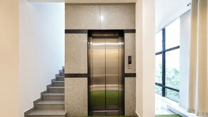 An elevator in a building with a staircase leading to it, a digital display, and a window with a view of greenery outside. - FabHotel Fabulous (Bangalore)