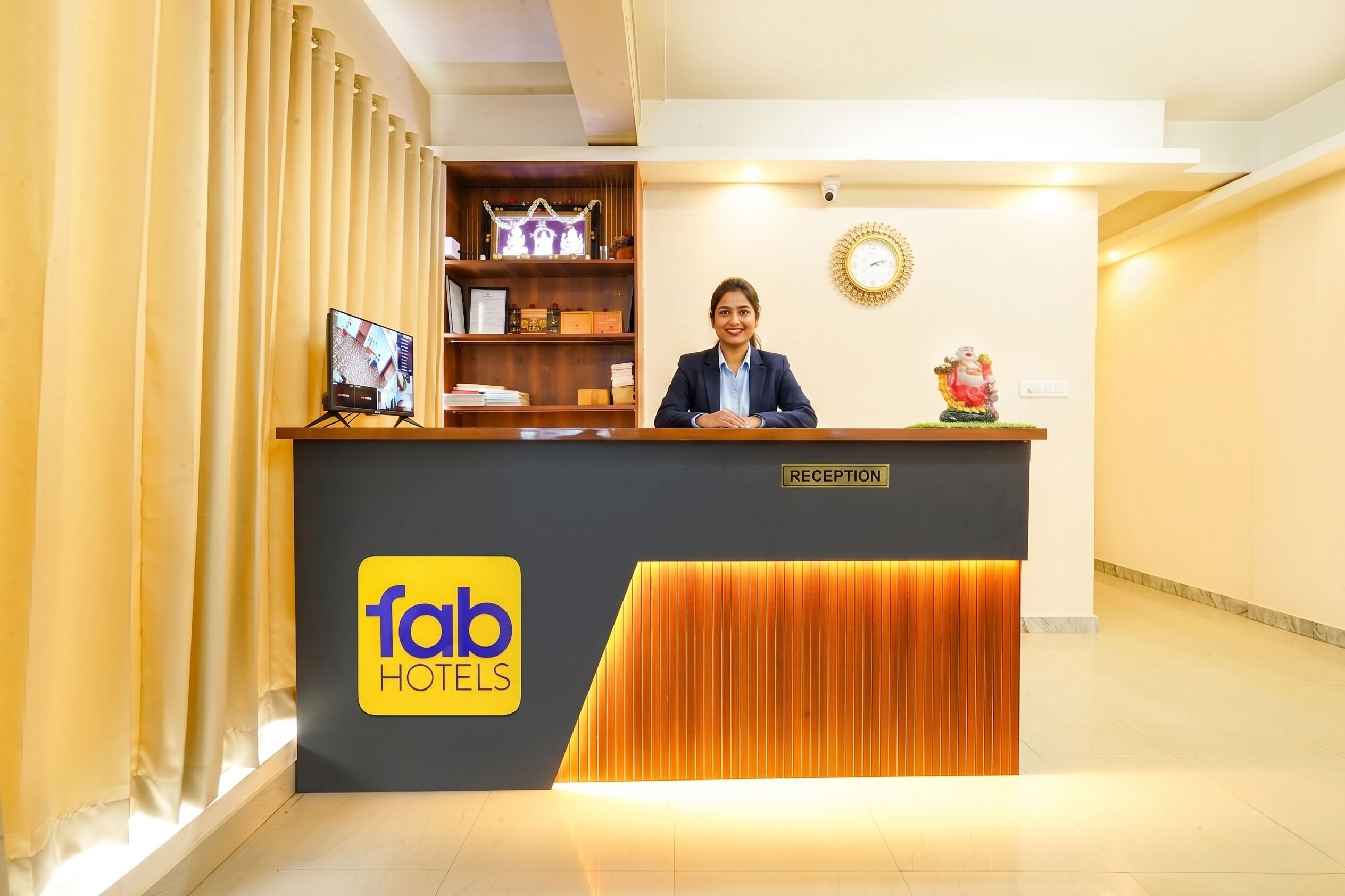 A reception desk with a 'fab hotels' logo, a clock, and a statue on the wall.
