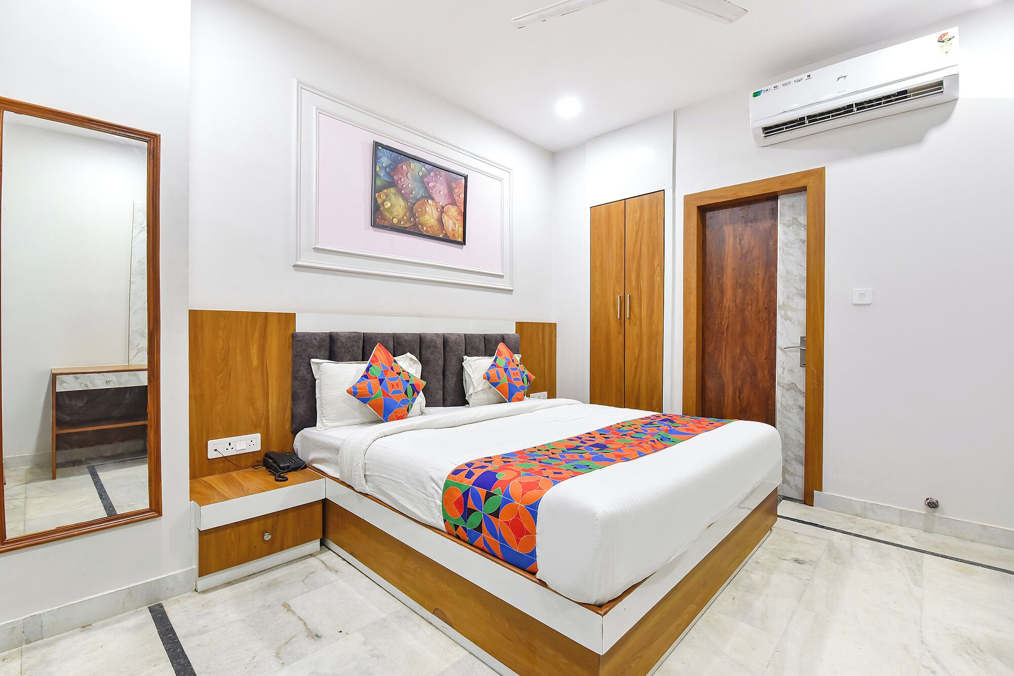 Un dormitorio con cama, mesitas de noche, armario, espejo y aire acondicionado.