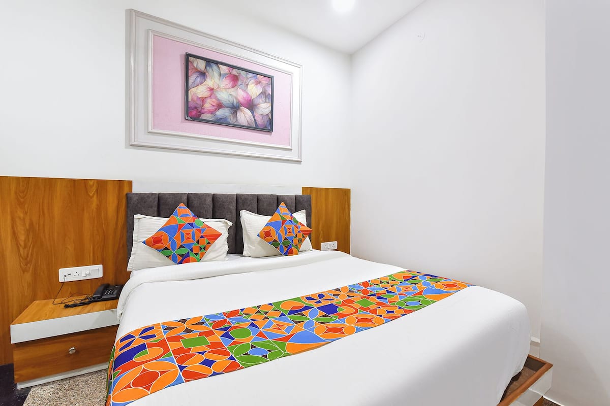 Ein Hotelzimmer mit Bett, Nachttisch, Telefon, Wandbild und Fenster.