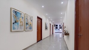 A hallway with framed abstract art, wooden doors, a clock, and a shelf with decorative items. - Fabhotel Rv (Noida)