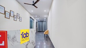 A hotel reception area with a marble floor, a reception desk, a ceiling fan, and framed notices on the wall. - Fabhotel Rv (Noida)