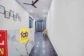 A hotel reception area with a marble floor, a reception desk, a ceiling fan, and framed notices on the wall. - Fabhotel Rv (Noida)